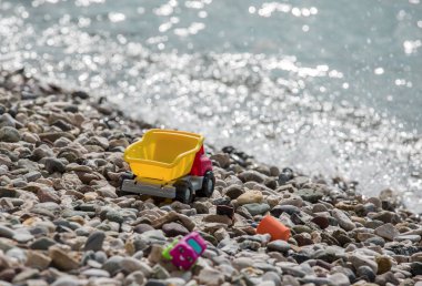 Bir çakıl plajı üzerinde parlak plastik küçük bebek oyuncak arabalar denize yakın. Yaz için bekliyor.
