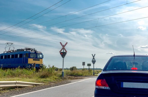 The electric train approaching railroad crossing. Car standing in front of the railway crossing with traffic light and road sign without a barrier