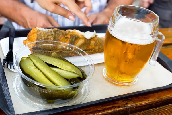 Delicioso pescado frito, pepinos en escabeche y vaso frío de cerveza de barril en una bandeja sobre una mesa de madera en la cafetería al aire libre —  Fotos de Stock