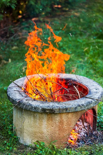 Torra grenar bränna i isolerade lägerelden grop i trädgården. Höga ljusa flammor flimmer på öppen trädgård eld grop — Stockfoto