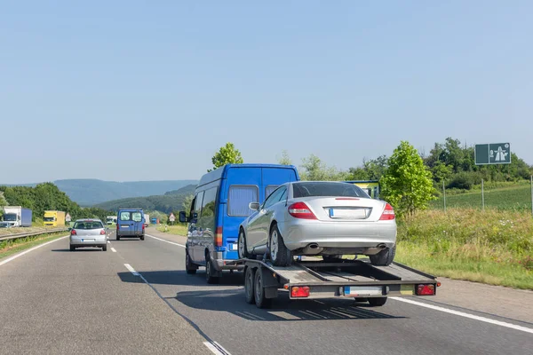 Arabalı bir karavan. Otoyolda araba taşıyan çekici taşıyan mavi minibüs..