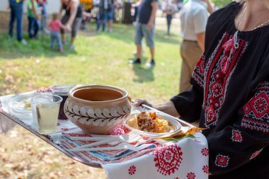 Kırmızı ve beyaz ipliklerle işlenmiş siyah ulusal bluzlu bir kadın. Elinde nakışlı havluyla bir tepsi tutuyor. Geleneksel Ukrayna yemeği çorbası ve tepside köfte.