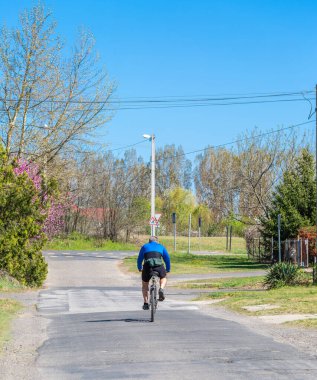Güneşli bir günde kırsal bir sokakta kasksız bisiklet süren bisikletçi.