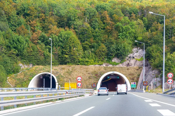 Hırvatistan dağlarında tünel girişi. Otostop çeken arabalarla dolu renkli bir manzara ve parlak sonbahar yapraklarıyla dağ ormanı.