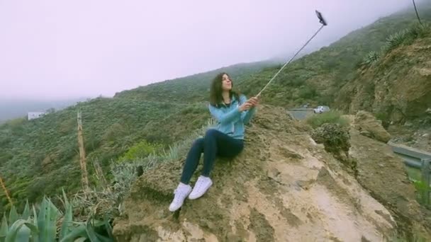 Chica toma un retrato en una roca en la selva usando un palo selfie — Vídeos de Stock