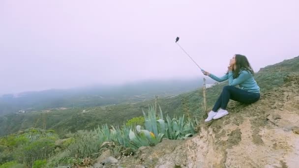 Chica utiliza un palo selfie en el fondo de rocas verdes de un volcán canario — Vídeos de Stock