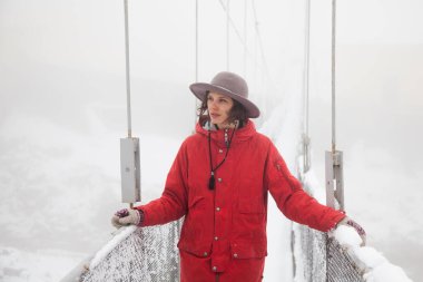 Kırmızı ceketli kız köprüde duruyor.