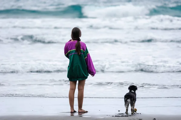 small dog with its owner dressed in a striking green and purple jacket on the beach on a cloudy day