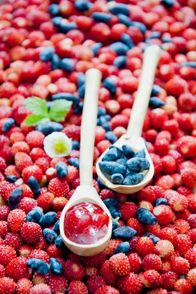 Wild berries Jam in a spoon, strawberries and Blue Honeysuckle Berries background