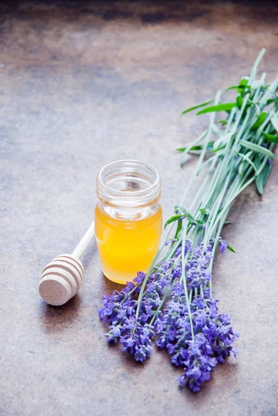 Jar of herbal honey surrounded by lavender flowers on a wooden background