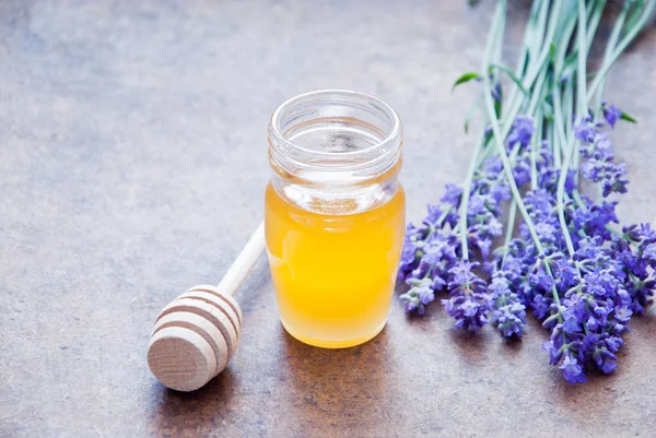 Jar of herbal honey surrounded by lavender flowers on a wooden background