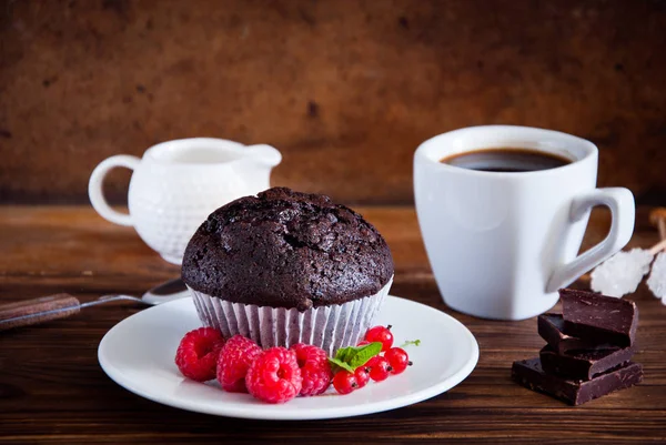 Muffin de chocolate com bagas vermelhas e xícara de café preto — Fotografia de Stock