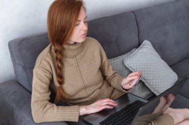 Bilgisayarı ve banka kartı olan beyaz bir kadın internette ödeme yapıyor..