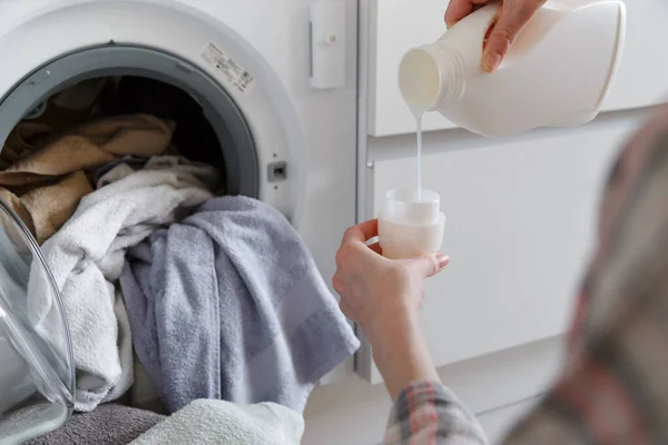 Primer plano de las manos femeninas vertiendo detergente líquido de lavandería en la tapa en la mesa rústica blanca con toallas en el fondo en el baño . — Foto de Stock