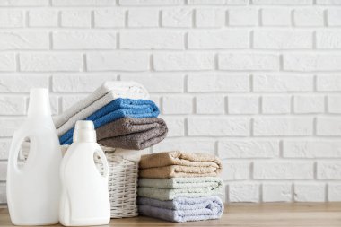Çamaşır konsepti. Deterjan jeli şişeler ve ahşap masadaki sepetin içinde yemyeşil havlular ve arka planda beyaz tuğla duvar..