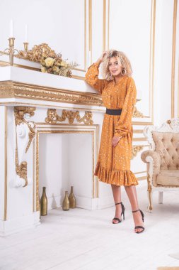 Genç ve güzel bir Afrikalı kadının portresi. Yazlık elbise içinde, şöminenin yanındaki lüks bir iç mekânda duruyor.