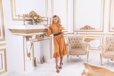 Genç ve güzel bir Afrikalı kadının portresi. Yazlık elbise içinde, şöminenin yanındaki lüks bir iç mekânda duruyor.