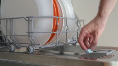 Adam bulaşık makinesine deterjan tableti koydu.