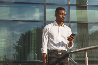 Cam duvarın önünde cep telefonu olan genç bir işadamı..