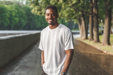 Parkta kameraya gülümseyen genç bir adam. Yatay çerçeveli çekim.