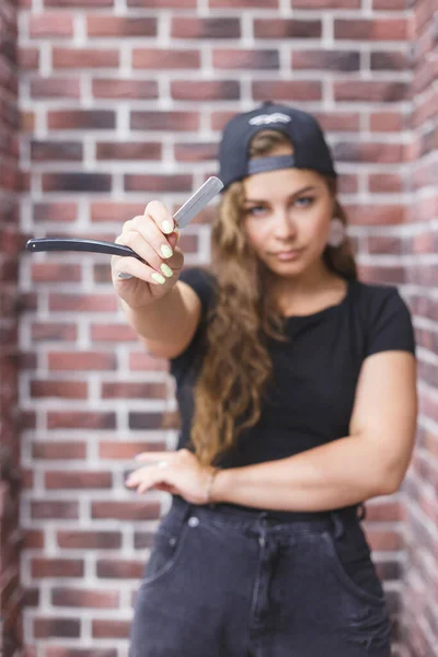 Young caucasian professional barber woman holding a straight razor standing against a brick wall