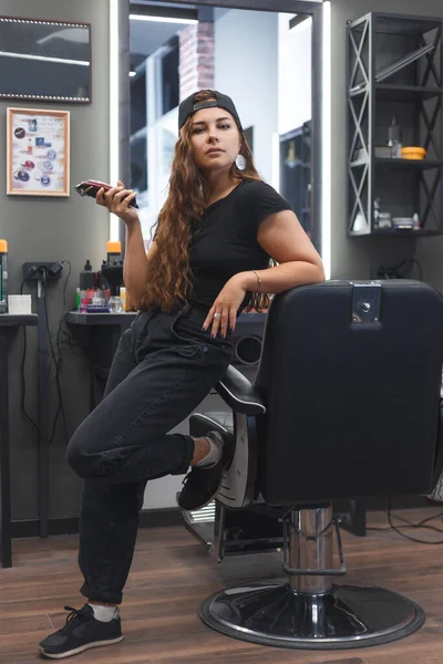 Young caucasian barber woman holding a clipper and standing at workplace