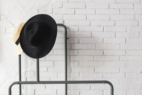 Black and white hat on hanger. White brick wall.