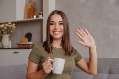Elinde kupayla kameraya bakıp el sallayan hoş bir genç kadının portresi. Güzel bir milenyum bayanı aileleriyle video bağlantısı kuruyor. Çekici kadın blogcu takipçileri selamlıyor.