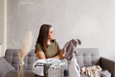 Genç kız yeni deterjan janıyla yıkadıktan sonra renkli şeyleri kontrol ediyor. Evdeki oturma odasında.