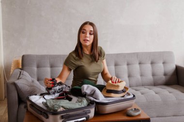 Kilitleme sürecinden sonraki tatil için bavul hazırlığı. Seyahatten önce evdeki kanepede giysileri ve eşyaları kontrol eden genç bir kadın.