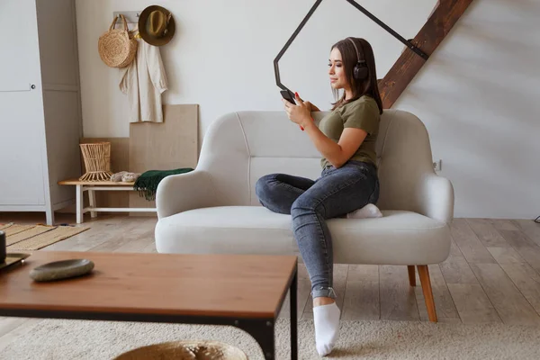 Jovencita alegre escuchando música en auriculares inalámbricos conectados a smartphone en apartamento loft — Foto de Stock