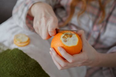 Close up view on women hand peeling an orange by segments with knife clipart