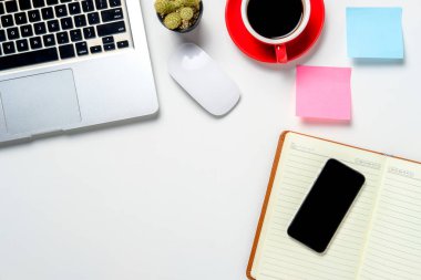 Yukarıdan bak. Laptop, fare, not defteri, not defteri, akıllı telefon ve beyaz ofis masasının üzerinde fotokopi alanı olan bir fincan kahve..