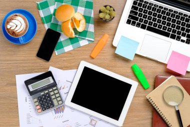 Laptop, dizüstü bilgisayar, not defteri, fırın, akıllı telefon, tablet, hesap makinesi, mali veri veya grafik ve kahve fincanı olan ofis masaüstü. Üst görünüm.
