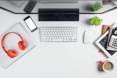 Bilgisayar, hesap makinesi, tablet, dizüstü bilgisayar, boş ekran akıllı telefon, kulaklık ve kahve içeren modern beyaz ofis masası. Kopya alanı olan üst görünüm. Çalışma masası konsepti.
