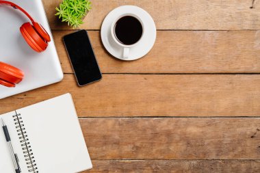 Bilgisayarlı ofis eşyaları, boş ekran akıllı telefon, kulaklık, defter ve kahve. Kopya alanlı üst görünüm. Çalışma masası konsepti..