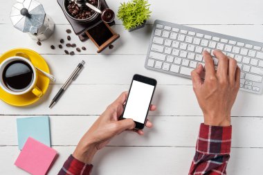 Adam elleri boş ekranı tutuyor akıllı telefonu ve çalışma alanı üzerinde bilgisayar kullanıyor. Grafiksel ekran montajı için.