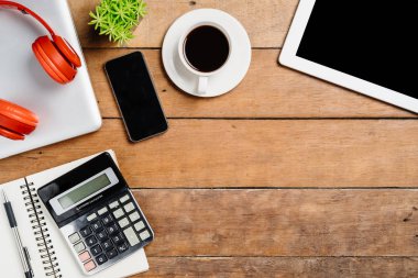 Bilgisayarlı ofis malzemeleri, boş ekran akıllı telefon, kulaklık, not defteri, tablet, hesap makinesi ve kahve fincanı. Kopya alanlı üst görünüm. Çalışma masası konsepti..