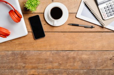 Bilgisayarlı ofis malzemeleri, boş ekran akıllı telefon, kulaklık, not defteri, tablet, hesap makinesi ve kahve fincanı. Kopya alanlı üst görünüm. Çalışma masası konsepti..