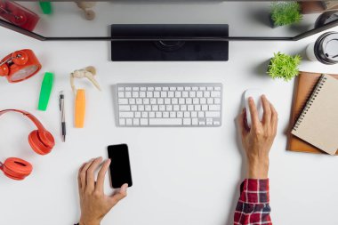 Adam elleri boş ekranı tutuyor akıllı telefonu ve çalışma alanı üzerinde bilgisayar kullanıyor. Grafiksel ekran montajı için.