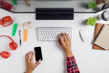Adam elleri boş ekranı tutuyor akıllı telefonu ve çalışma alanı üzerinde bilgisayar kullanıyor. Grafiksel ekran montajı için