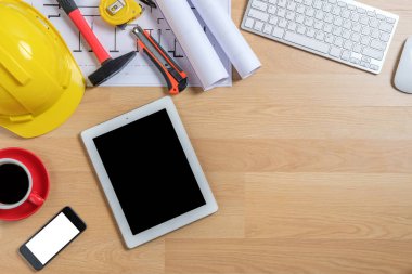 Bilgisayarlı ofis masası, akıllı telefon, tablet, bir fincan kahve ve mühendis teçhizatı. Arkaplan inşa projesi fikri.