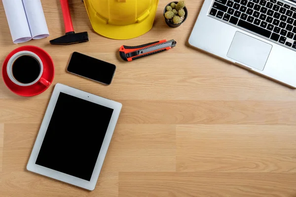Bilgisayarlı ofis masası, akıllı telefon, tablet, bir fincan kahve ve mühendis teçhizatı. Arkaplan inşa projesi fikri.