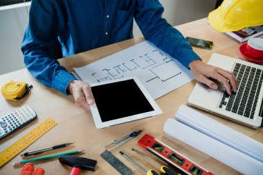 Mühendis el, ofisteki inşaat alanında tablet ve dizüstü bilgisayarla mimari proje üzerinde çalışıyor..