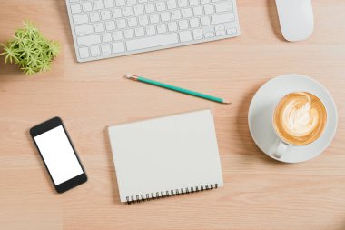 Yukarıdan görünüm. Klavye, fare, kalem, defter, akıllı telefon ve bir fincan kahve..