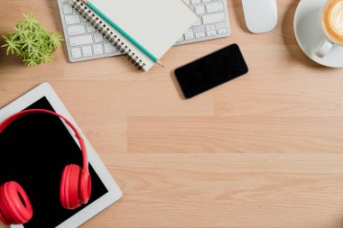 Yukarıdan görünüm. Klavye, fare, kalem, not defteri, akıllı telefon, kulaklık, tablet ve kahve fotokopi alanı ile ofis masasında..