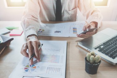 Akıllı telefon ve finansal veriler ve dizüstü bilgisayarla çalışan bir iş adamı ofisteki modern beyaz masada. İş analizi ve strateji kavramı.