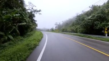 Ağır çekim. Sarı işaretlerle asfalt yolda ilerlerken yağmur sisli tropikal yağmur ormanları dağının içinden geçiyor..