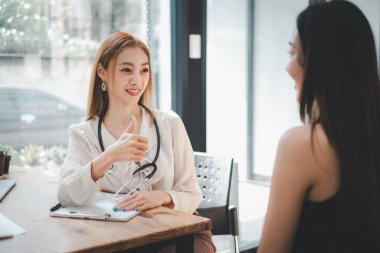Gülümseyen bir sağlık çalışanı, iyi ışıklandırılmış, modern bir ofisteki bir müşteriyle yapılan olumlu istişare sırasında onay veriyor..
