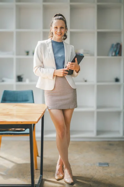 Professional and approachable businesswoman using a tablet in her well-organized office workspace.